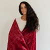 A woman is wrapped in a red luxurious patterned faux fur throw blanket that is a Saranoni blanket. This ultra-soft, plush throw blanket adds a touch of elegance and warmth to any space, perfect as a soft throw blanket or fluffy blanket for lounging. Ideal for those seeking a high-quality artificial fur blanket or luxury blanket, this versatile and stylish soft blanket enhances both comfort and decor. Shop the best blankets and throws for ultimate relaxation and cozy vibes.