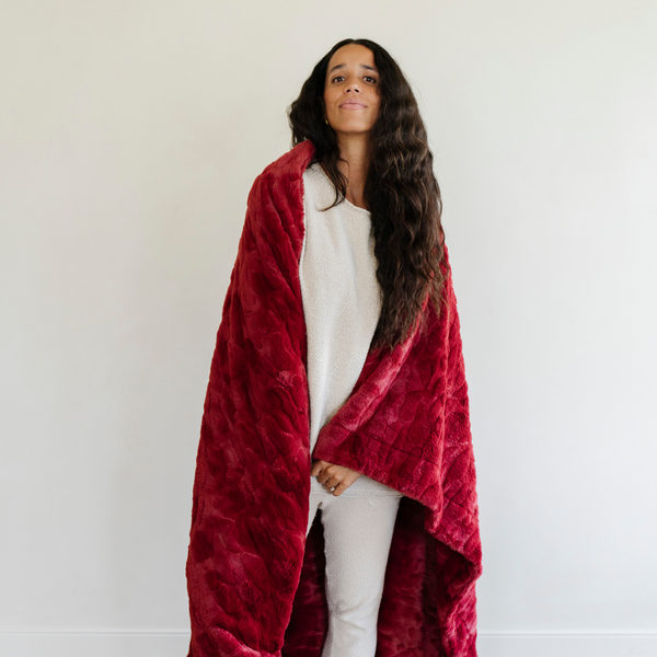 A woman is wrapped in red luxurious patterned faux fur extra large throw blanket that is a Saranoni blanket. This ultra-soft, cozy blanket adds a touch of elegance and warmth to any space, perfect as a soft oversized blanket or fluffy blanket for lounging. Ideal for those seeking a high-quality artificial fur blanket or luxury blanket, this versatile and stylish soft blanket enhances both comfort and decor. Shop the best blankets and throws for ultimate relaxation and cozy vibes.