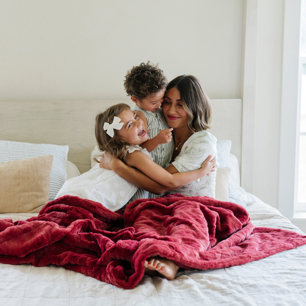 A mother and her son and daughter have a red luxurious patterned faux fur extra large throw blanket that is a Saranoni blanket. This ultra-soft, cozy blanket adds a touch of elegance and warmth to any space, perfect as a soft oversized blanket or fluffy blanket for lounging. Ideal for those seeking a high-quality artificial fur blanket or luxury blanket, this versatile and stylish soft blanket enhances both comfort and decor. Shop the best blankets and throws for ultimate relaxation and cozy vibes.