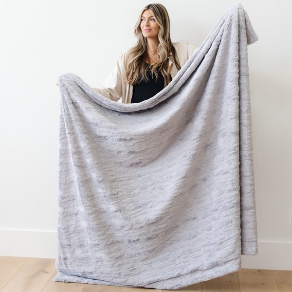 A woman holds a light gray luxurious patterned faux fur throw blanket that is a Saranoni blanket. This ultra-soft, plush throw blanket adds a touch of elegance and warmth to any space, perfect as a soft throw blanket or fluffy blanket for lounging. Ideal for those seeking a high-quality artificial fur blanket or luxury blanket, this versatile and stylish soft blanket enhances both comfort and decor. Shop the best blankets and throws for ultimate relaxation and cozy vibes.