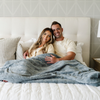 A husband and wife sit with a dusty blue luxurious patterned faux fur extra large throw blanket that is a Saranoni blanket. This ultra-soft, cozy blanket adds a touch of elegance and warmth to any space, perfect as a soft oversized blanket or fluffy blanket for lounging. Ideal for those seeking a high-quality artificial fur blanket or luxury blanket, this versatile and stylish soft blanket enhances both comfort and decor. Shop the best blankets and throws for ultimate relaxation and cozy vibes.