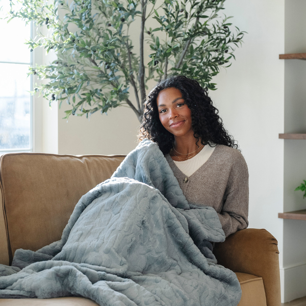 A woman holds a dusty blue luxurious patterned faux fur throw blanket that is a Saranoni blanket. This ultra-soft, plush throw blanket adds a touch of elegance and warmth to any space, perfect as a soft throw blanket or fluffy blanket for lounging. Ideal for those seeking a high-quality artificial fur blanket or luxury blanket, this versatile and stylish soft blanket enhances both comfort and decor. Shop the best blankets and throws for ultimate relaxation and cozy vibes.