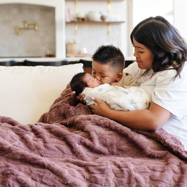 A mother and her two little boys and a dusty mauve luxurious patterned faux fur extra large throw blanket that is a Saranoni blanket. This ultra-soft, cozy blanket adds a touch of elegance and warmth to any space, perfect as a soft oversized blanket or fluffy blanket for lounging. Ideal for those seeking a high-quality artificial fur blanket or luxury blanket, this versatile and stylish soft blanket enhances both comfort and decor. Shop the best blankets and throws for ultimate relaxation and cozy vibes.