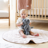 A curious toddler sits on a soft quilt, hugging a gray elephant stuffed animal. Dressed in a cute outfit, the child gazes at the camera, surrounded by a cozy nursery setting with a crib and soft blankets in the background. This heartwarming scene captures the joy of childhood and the comfort of cuddling with plush toys, perfect for nurturing imaginative play.