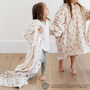 Two young girls smiling while one is wrapped in 'Elf' holiday-themed blanket with a fun pattern featuring Buddy the Elf and Christmas-themed icons and the other is wearing an 'Elf' snuggler with the same pattern. Perfect for bringing festive joy and comfort to the holiday season. The soft blanket is a luxury blanket and a Saranoni blanket. 