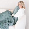 A woman smiles and holds a eucalyptus colored luxurious patterned faux fur extra large throw blanket that is a Saranoni blanket. This ultra-soft, cozy blanket adds a touch of elegance and warmth to any space, perfect as a soft oversized blanket or fluffy blanket for lounging. Ideal for those seeking a high-quality artificial fur blanket or luxury blanket, this versatile and stylish soft blanket enhances both comfort and decor. Shop the best blankets and throws for ultimate relaxation and cozy vibes.