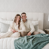 A husband and wife sit by a eucalyptus luxurious patterned faux fur throw blanket that is a Saranoni blanket. This ultra-soft, plush throw blanket adds a touch of elegance and warmth to any space, perfect as a soft throw blanket or fluffy blanket for lounging. Ideal for those seeking a high-quality artificial fur blanket or luxury blanket, this versatile and stylish soft blanket enhances both comfort and decor. Shop the best blankets and throws for ultimate relaxation and cozy vibes.