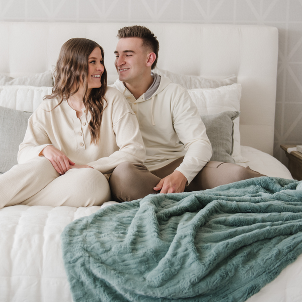 A husband and wife sit by a eucalyptus colored luxurious patterned faux fur extra large throw blanket that is a Saranoni blanket. This ultra-soft, cozy blanket adds a touch of elegance and warmth to any space, perfect as a soft oversized blanket or fluffy blanket for lounging. Ideal for those seeking a high-quality artificial fur blanket or luxury blanket, this versatile and stylish soft blanket enhances both comfort and decor. Shop the best blankets and throws for ultimate relaxation and cozy vibes.