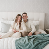 A husband and wife sit by a eucalyptus colored luxurious patterned faux fur extra large throw blanket that is a Saranoni blanket. This ultra-soft, cozy blanket adds a touch of elegance and warmth to any space, perfect as a soft oversized blanket or fluffy blanket for lounging. Ideal for those seeking a high-quality artificial fur blanket or luxury blanket, this versatile and stylish soft blanket enhances both comfort and decor. Shop the best blankets and throws for ultimate relaxation and cozy vibes.