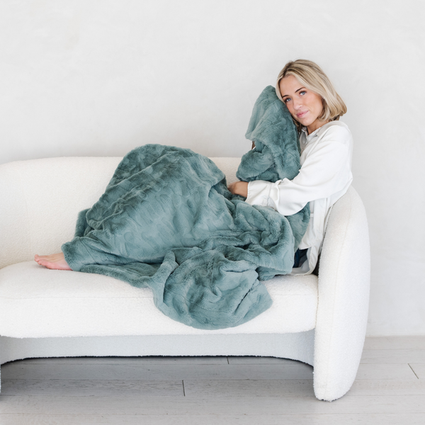 A woman holds a eucalyptus luxurious patterned faux fur throw blanket that is a Saranoni blanket. This ultra-soft, plush throw blanket adds a touch of elegance and warmth to any space, perfect as a soft throw blanket or fluffy blanket for lounging. Ideal for those seeking a high-quality artificial fur blanket or luxury blanket, this versatile and stylish soft blanket enhances both comfort and decor. Shop the best blankets and throws for ultimate relaxation and cozy vibes.