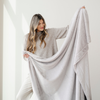 A woman smiles and holds up a light gray blanket that is a luxury blanket and a Saranoni blanket. This soft blanket is also a lush blanket. This cozy blanket is perfect for gifting, relaxing, or as a home decor staple. Enjoy this extra large throw blanket for years to come!