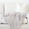 A gorgeous light gray blanket is draped on a cream couch. This soft blanket is a lush blanket and a Saranoni blanket. This luxury blanket is such a cozy blanket and is great for relaxing, gifting, or as a home decor staple. Enjoy this extra large blanket for years to come. 