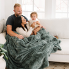 A husband and wife with their little girl and a dusty green luxurious patterned faux fur throw blanket that is a Saranoni blanket. This ultra-soft, plush throw blanket adds a touch of elegance and warmth to any space, perfect as a soft throw blanket or fluffy blanket for lounging. Ideal for those seeking a high-quality artificial fur blanket or luxury blanket, this versatile and stylish soft blanket enhances both comfort and decor. Shop the best blankets and throws for ultimate relaxation and cozy vibes.