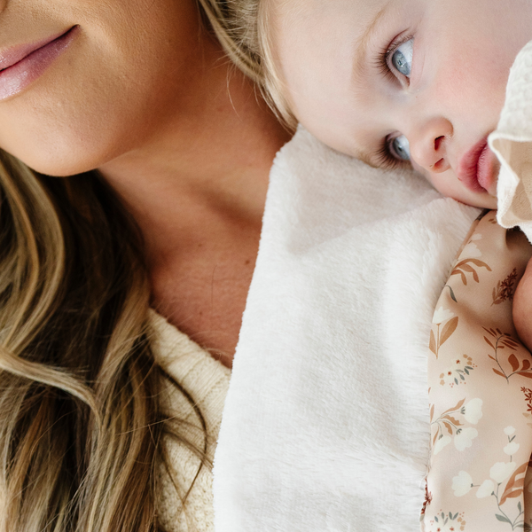 Mom and daughter laying with a white and tan floral mini blanket. 