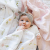 A little girl lies on a luxuriously soft, reversible muslin quilt. The soft blanket is a luxury blanket and a lightweight and airy baby blanket as well as a Saranoni blanket. One side of the baby quilt features a delicate floral print with soft pink trim, while the reverse showcases a blush pink dotted pattern. This ultra-soft, baby blanket is perfect for snuggles, tummy time, stroller rides, or nursery decor, making it an essential for newborns, infants, and toddlers.