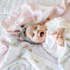 A happy baby girl lies on a luxuriously soft, reversible muslin quilt. The soft blanket is a luxury blanket and a lightweight and airy baby blanket as well as a Saranoni blanket. One side of the baby quilt features a delicate floral print with soft pink trim, while the reverse showcases a blush pink dotted pattern. This ultra-soft, baby blanket is perfect for snuggles, tummy time, stroller rides, or nursery decor, making it an essential for newborns, infants, and toddlers.