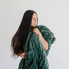 Woman holds a luxurious green double ruched holiday blanket, showcasing its plush, soft texture. Perfect cozy accessory for winter and holiday season styling.The soft blanket is a luxury blanket and a Saranoni blanket. 