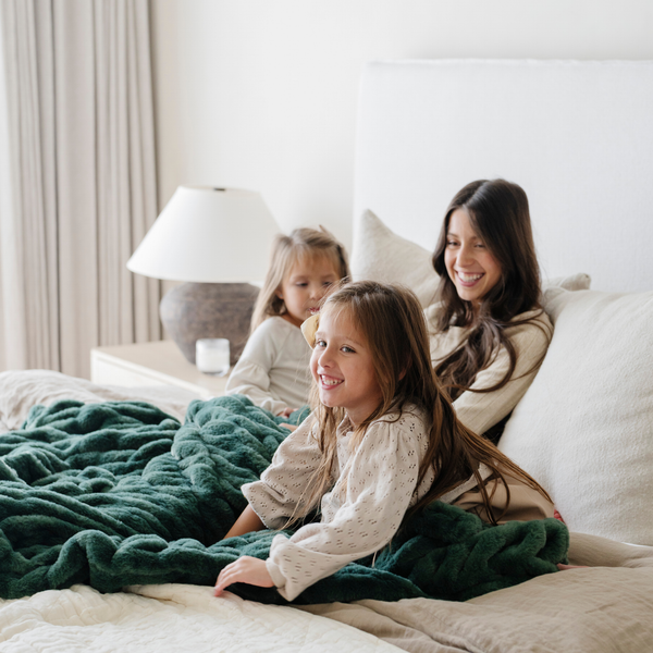 Smiling family cuddled together on a bed with a plush green double ruched holiday blanket, creating cozy family moments perfect for the winter season. Ideal for holiday decor and relaxation. The soft blanket is a luxury blanket. 