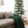 Plush green double ruched blanket draped over a sofa beside a Christmas tree and presents, creating a cozy, festive atmosphere in the living room. Ideal for holiday home decor and winter warmth. The soft blanket is a luxury blanket and a Saranoni blanket. 