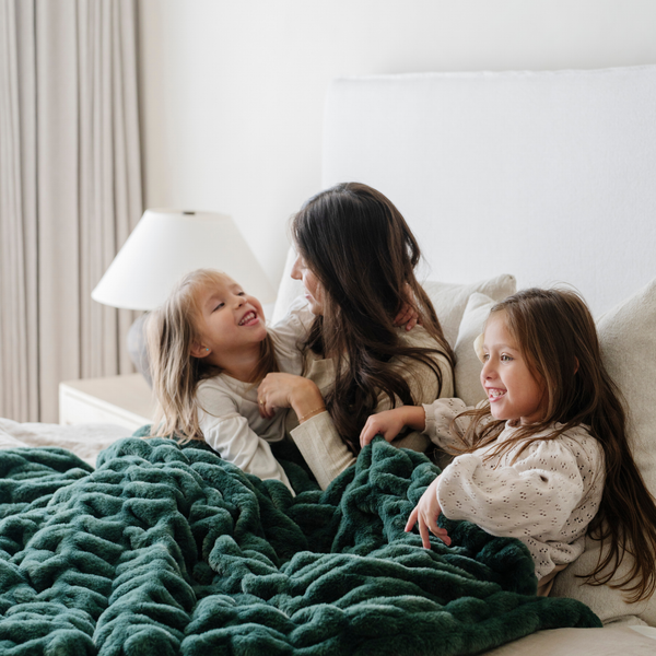 Smiling family cuddled together on a bed with a plush green double ruched holiday blanket, creating cozy family moments perfect for the winter season. Ideal for holiday decor and relaxation. The soft blanket is a luxury blanket. 