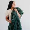 Woman holds a luxurious green double ruched holiday blanket, showcasing its plush, soft texture. Perfect cozy accessory for winter and holiday season styling.The soft blanket is a luxury blanket and a Saranoni blanket. 