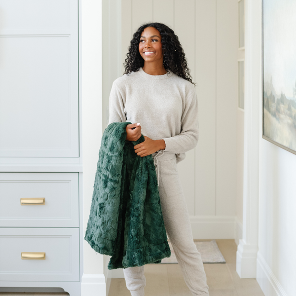 A woman smiles and holds a green luxurious patterned faux fur throw blanket that is a Saranoni blanket. This ultra-soft, plush throw blanket adds a touch of elegance and warmth to any space, perfect as a soft throw blanket or fluffy blanket for lounging. Ideal for those seeking a high-quality artificial fur blanket or luxury blanket, this versatile and stylish soft blanket enhances both comfort and decor. Shop the best blankets and throws for ultimate relaxation and cozy vibes.