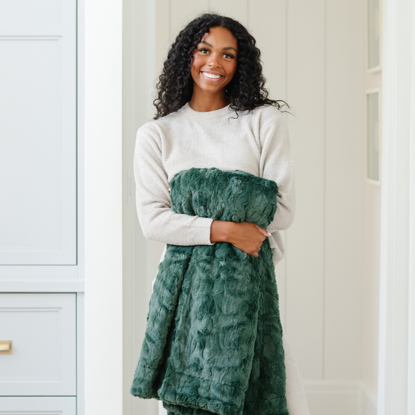 A woman smiles and holds a green luxurious patterned faux fur throw blanket that is a Saranoni blanket. This ultra-soft, plush throw blanket adds a touch of elegance and warmth to any space, perfect as a soft throw blanket or fluffy blanket for lounging. Ideal for those seeking a high-quality artificial fur blanket or luxury blanket, this versatile and stylish soft blanket enhances both comfort and decor. Shop the best blankets and throws for ultimate relaxation and cozy vibes.