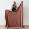 A woman holds up a Bamboni® blanket by Saranoni. This ultra-soft blanket is a clay colored blanket and made from a premium blend of bamboo rayon and poly microfiber, offering a lightweight, breathable, and fluffy feel. Perfect as a extra large blanket, luxury blanket, or soft blanket, it adds warmth and elegance to any living room, bedroom, or home décor setting. Designed for ultimate comfort, this buttery-soft Saranoni blanket is ideal for gifting. Enjoy this cozy blanket for years to come!