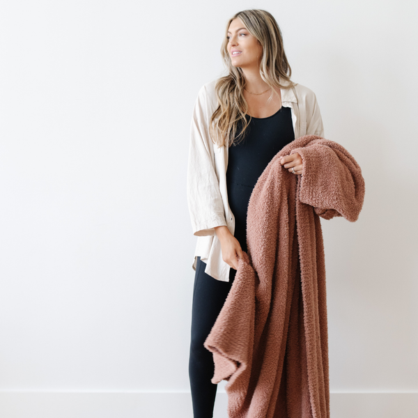 A woman holds a Bamboni® blanket by Saranoni. This ultra-soft blanket is a clay colored blanket and made from a premium blend of bamboo rayon and poly microfiber, offering a lightweight, breathable, and fluffy feel. Perfect as a extra large blanket, luxury blanket, or soft blanket, it adds warmth and elegance to any living room, bedroom, or home décor setting. Designed for ultimate comfort, this buttery-soft Saranoni blanket is ideal for gifting. Enjoy this cozy blanket for years to come!