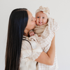 A mother holds her baby girl in a Minky Stretch Luxe swaddle in gingham pattern, featuring ultra-soft minky fabric with a luxurious stretch, perfect for keeping your baby cozy and comfortable. Ideal for newborns and infants.This soft swaddle is a luxury swaddle and a Saranoni swaddle. 