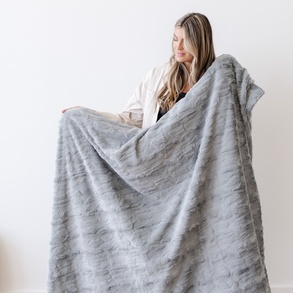 A woman holds a gray luxurious patterned faux fur throw blanket that is a Saranoni blanket. This ultra-soft, plush throw blanket adds a touch of elegance and warmth to any space, perfect as a soft throw blanket or fluffy blanket for lounging. Ideal for those seeking a high-quality artificial fur blanket or luxury blanket, this versatile and stylish soft blanket enhances both comfort and decor. Shop the best blankets and throws for ultimate relaxation and cozy vibes.