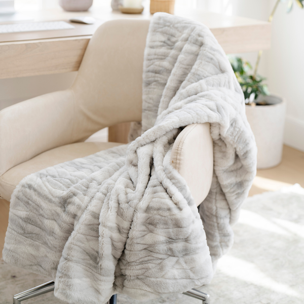 Draped over a chair is a Saranoni blanket, specifically the gray marbled faux fur/minky extra large blanket, highlighting its ultra-soft texture and luxurious design. This plush blanket features a dual-texture blend of silky minky and cozy faux fur, creating the ultimate cozy blanket for home decor. Perfect luxury blanket for lounging or adding style to any space. Soft blanket, cozy blanket—experience unmatched warmth with a Saranoni blanket. 