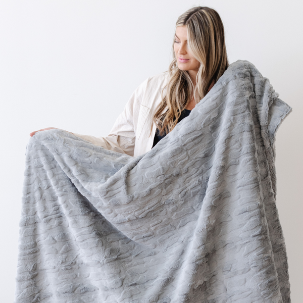 A woman holds a gray luxurious patterned faux fur extra large throw blanket that is a Saranoni blanket. This ultra-soft, cozy blanket adds a touch of elegance and warmth to any space, perfect as a soft oversized blanket or fluffy blanket for lounging. Ideal for those seeking a high-quality artificial fur blanket or luxury blanket, this versatile and stylish soft blanket enhances both comfort and decor. Shop the best blankets and throws for ultimate relaxation and cozy vibes.