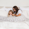 A mother and her daughter smile and sit with a luxurious double-layer Bamboni® blanket by Saranoni, featuring gray leopard print that is white and gray. This ultra-soft blanket is crafted from bamboo rayon and poly microfiber, making it lightweight, breathable, and fluffy. Ideal as a cozy throw blanket, luxury blanket, plush throw, soft blanket, or stylish home accent, this Saranoni blanket brings warmth, comfort, and timeless elegance to any living room or bedroom.