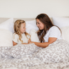 A mother and her daughter sit with a luxurious double-layer Bamboni® blanket by Saranoni, featuring gray leopard print that is white and gray. This ultra-soft blanket is crafted from bamboo rayon and poly microfiber, making it lightweight, breathable, and fluffy. Ideal as a cozy throw blanket, luxury blanket, plush throw, soft blanket, or stylish home accent, this Saranoni blanket brings warmth, comfort, and timeless elegance to any living room or bedroom.