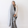 A woman holds a gray luxurious patterned faux fur extra large throw blanket that is a Saranoni blanket. This ultra-soft, cozy blanket adds a touch of elegance and warmth to any space, perfect as a soft oversized blanket or fluffy blanket for lounging. Ideal for those seeking a high-quality artificial fur blanket or luxury blanket, this versatile and stylish soft blanket enhances both comfort and decor. Shop the best blankets and throws for ultimate relaxation and cozy vibes.