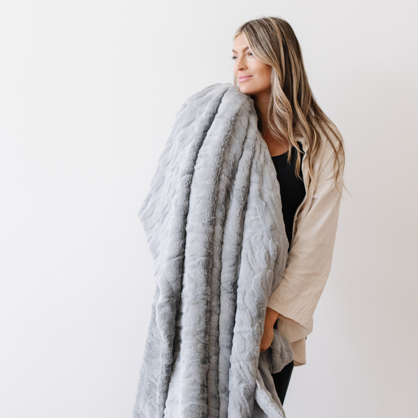 A woman holds a gray luxurious patterned faux fur throw blanket that is a Saranoni blanket. This ultra-soft, plush throw blanket adds a touch of elegance and warmth to any space, perfect as a soft throw blanket or fluffy blanket for lounging. Ideal for those seeking a high-quality artificial fur blanket or luxury blanket, this versatile and stylish soft blanket enhances both comfort and decor. Shop the best blankets and throws for ultimate relaxation and cozy vibes.