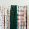 Three holiday patterned blankets. One with holly berries, one that is plaid, and one with Christmas illustrations (present, stockings, trees, bells, and some red dots). The soft blankets are luxury blankets. The other side of the blankets is either a Christmas green or an ivory.