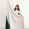 Woman holding an extra large holiday blanket with a holly berry print and green backing, showcasing the blanket’s soft and cozy texture. Great for winter home decor and holiday gifting. The soft blanket is a luxury blanket and a Christmas blanket. 