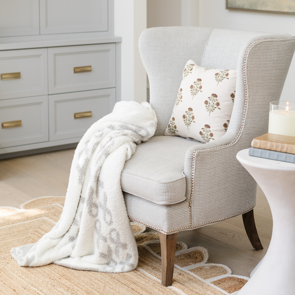 A luxurious double-layer Bamboni® blanket by Saranoni, featuring a white and gray blanket with a cancer ribbon pattern on it draped on a chair. This ultra-soft blanket is crafted from bamboo rayon and poly microfiber, making it lightweight, breathable, and fluffy. Ideal as a cozy throw blanket, luxury blanket, plush throw, soft blanket, or stylish home accent, this Saranoni blanket brings warmth, comfort, and timeless elegance to any living room or bedroom.