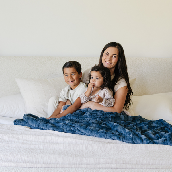 A mother and her son and daughter sit with a blue luxurious patterned faux fur throw blanket that is a Saranoni blanket. This ultra-soft, plush throw blanket adds a touch of elegance and warmth to any space, perfect as a soft throw blanket or fluffy blanket for lounging. Ideal for those seeking a high-quality artificial fur blanket or luxury blanket, this versatile and stylish soft blanket enhances both comfort and decor. Shop the best blankets and throws for ultimate relaxation and cozy vibes.