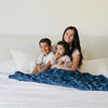 A mother and her son and daughter sit with a blue luxurious patterned faux fur extra large throw blanket that is a Saranoni blanket. This ultra-soft, cozy blanket adds a touch of elegance and warmth to any space, perfect as a soft oversized blanket or fluffy blanket for lounging. Ideal for those seeking a high-quality artificial fur blanket or luxury blanket, this versatile and stylish soft blanket enhances both comfort and decor. Shop the best blankets and throws for ultimate relaxation and cozy vibes.