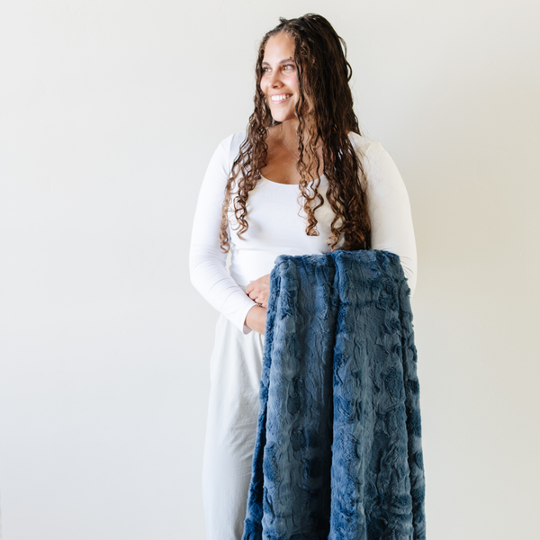 A woman holds a blue luxurious patterned faux fur throw blanket that is a Saranoni blanket. This ultra-soft, plush throw blanket adds a touch of elegance and warmth to any space, perfect as a soft throw blanket or fluffy blanket for lounging. Ideal for those seeking a high-quality artificial fur blanket or luxury blanket, this versatile and stylish soft blanket enhances both comfort and decor. Shop the best blankets and throws for ultimate relaxation and cozy vibes.