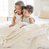 A brother and sister sit with a ivory colored extra large patterned faux fur throw Saranoni Luxury Blanket. The soft blanket is an oversized throw blanket.