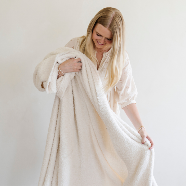 A woman smiles and holds a Bamboni® blanket by Saranoni. This ultra-soft blanket is a ivory blanket and made from a premium blend of bamboo rayon and poly microfiber, offering a lightweight, breathable, and fluffy feel. Perfect as a throw blanket, luxury blanket, plush throw, or soft blanket, it adds warmth and elegance to any living room, bedroom, or home décor setting. Designed for ultimate comfort, this buttery-soft Saranoni blanket is ideal for gifting. Enjoy this cozy blanket for years to come! 