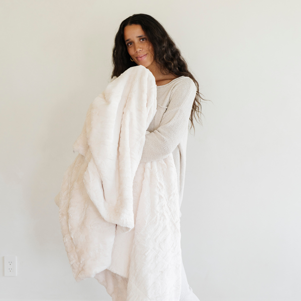 A woman holds a ivory luxurious patterned faux fur extra large throw blanket that is a Saranoni blanket. This ultra-soft, cozy blanket adds a touch of elegance and warmth to any space, perfect as a soft oversized blanket or fluffy blanket for lounging. Ideal for those seeking a high-quality artificial fur blanket or luxury blanket, this versatile and stylish soft blanket enhances both comfort and decor. Shop the best blankets and throws for ultimate relaxation and cozy vibes.