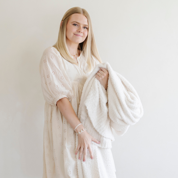 A woman holds a Bamboni® blanket by Saranoni. This ultra-soft blanket is a ivory blanket and made from a premium blend of bamboo rayon and poly microfiber, offering a lightweight, breathable, and fluffy feel. Perfect as a throw blanket, luxury blanket, plush throw, or soft blanket, it adds warmth and elegance to any living room, bedroom, or home décor setting. Designed for ultimate comfort, this buttery-soft Saranoni blanket is ideal for gifting. Enjoy this cozy blanket for years to come! 