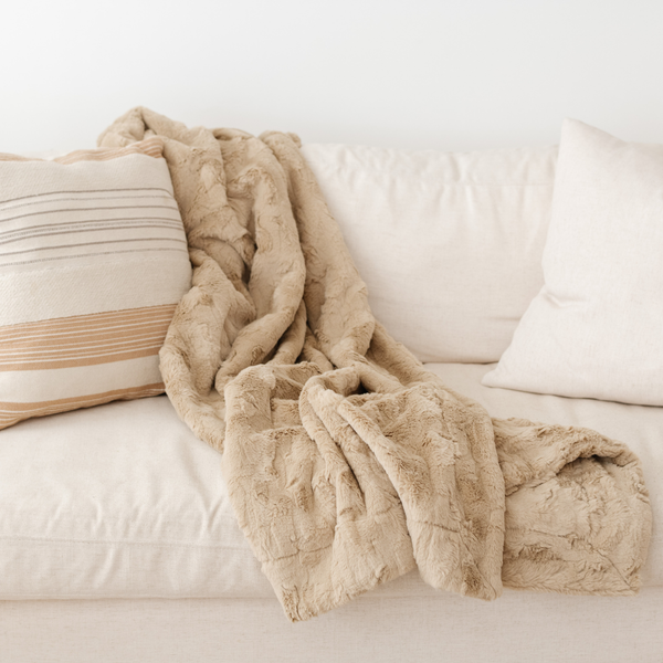 A khaki luxurious patterned faux fur throw blanket that is a Saranoni blanket is draped on a couch. This ultra-soft, plush throw blanket adds a touch of elegance and warmth to any space, perfect as a soft throw blanket or fluffy blanket for lounging. Ideal for those seeking a high-quality artificial fur blanket or luxury blanket, this versatile and stylish soft blanket enhances both comfort and decor. Shop the best blankets and throws for ultimate relaxation and cozy vibes.