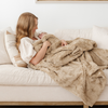 A mother holds her little girl and has a khaki luxurious patterned faux fur extra large throw blanket that is a Saranoni blanket. This ultra-soft, cozy blanket adds a touch of elegance and warmth to any space, perfect as a soft oversized blanket or fluffy blanket for lounging. Ideal for those seeking a high-quality artificial fur blanket or luxury blanket, this versatile and stylish soft blanket enhances both comfort and decor. Shop the best blankets and throws for ultimate relaxation and cozy vibes.