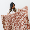 A woman holds up a luxurious double-layer Bamboni® blanket by Saranoni, featuring a chic burnt orange and cream geometric pattern. This ultra-soft blanket is crafted from bamboo rayon and poly microfiber, making it lightweight, breathable, and fluffy. Ideal as a cozy blanket, extra large blanket, luxury blanket, soft blanket, or stylish home accent, this Saranoni blanket brings warmth, comfort, and timeless elegance to any living room or bedroom.